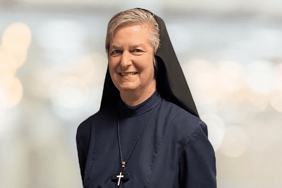 A nun in a traditional habit smiling gently with a blurred light background.