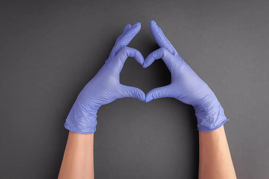 Two hands wearing blue latex gloves forming a heart shape against a grey background.