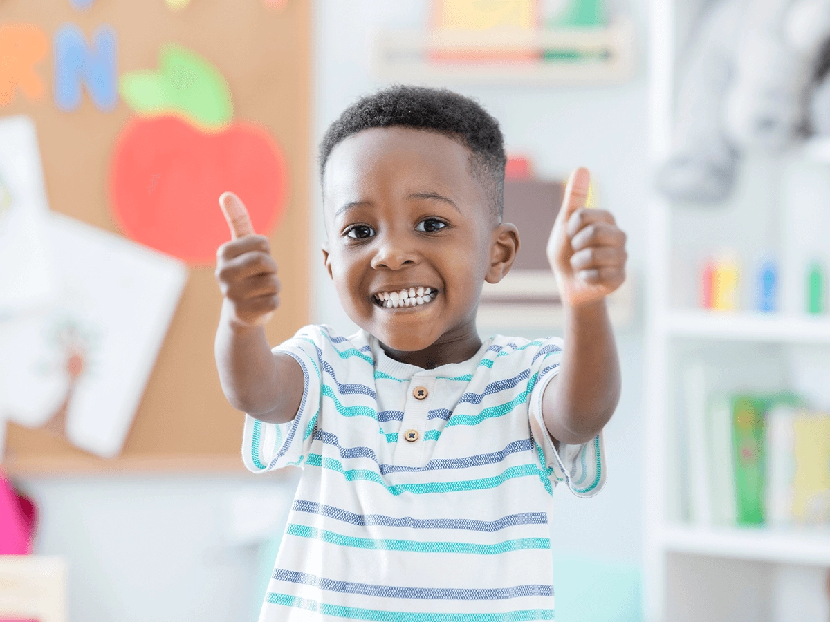 A young boy giving two thumbs up in his room.