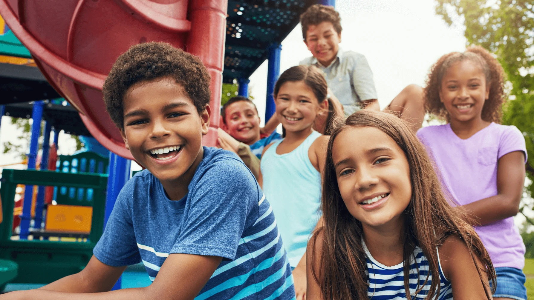 Group of happy children of diverse ethnicities playing on a playground, smiling at the camera.
