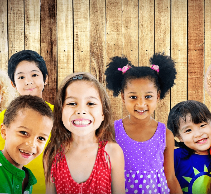A group of five diverse children smiling in front of a wooden backdrop.
