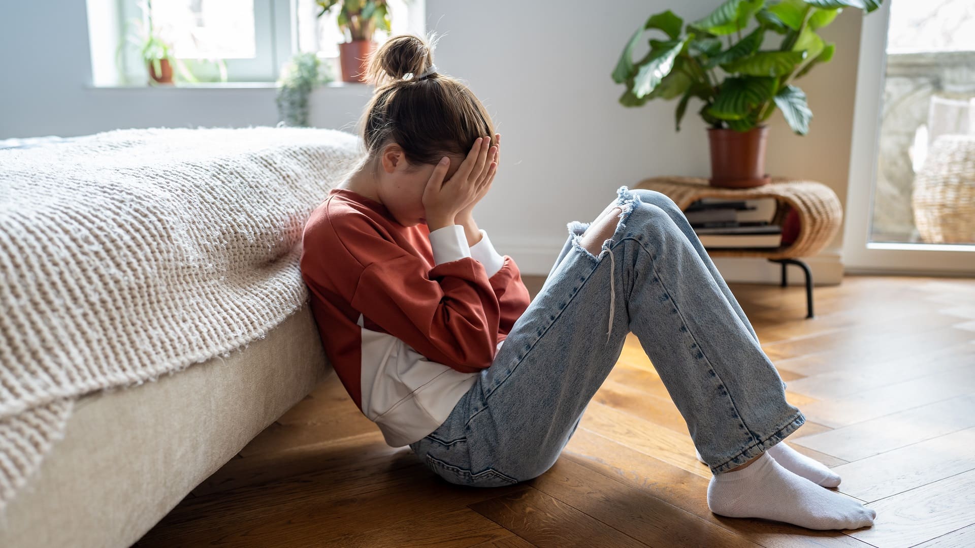 Unhappy teen girl covering face with hands and crying while sitting on floor with mobile phone nearby, upset frustrated child teenager being bullied or harassed online. Cyberbullying among teens